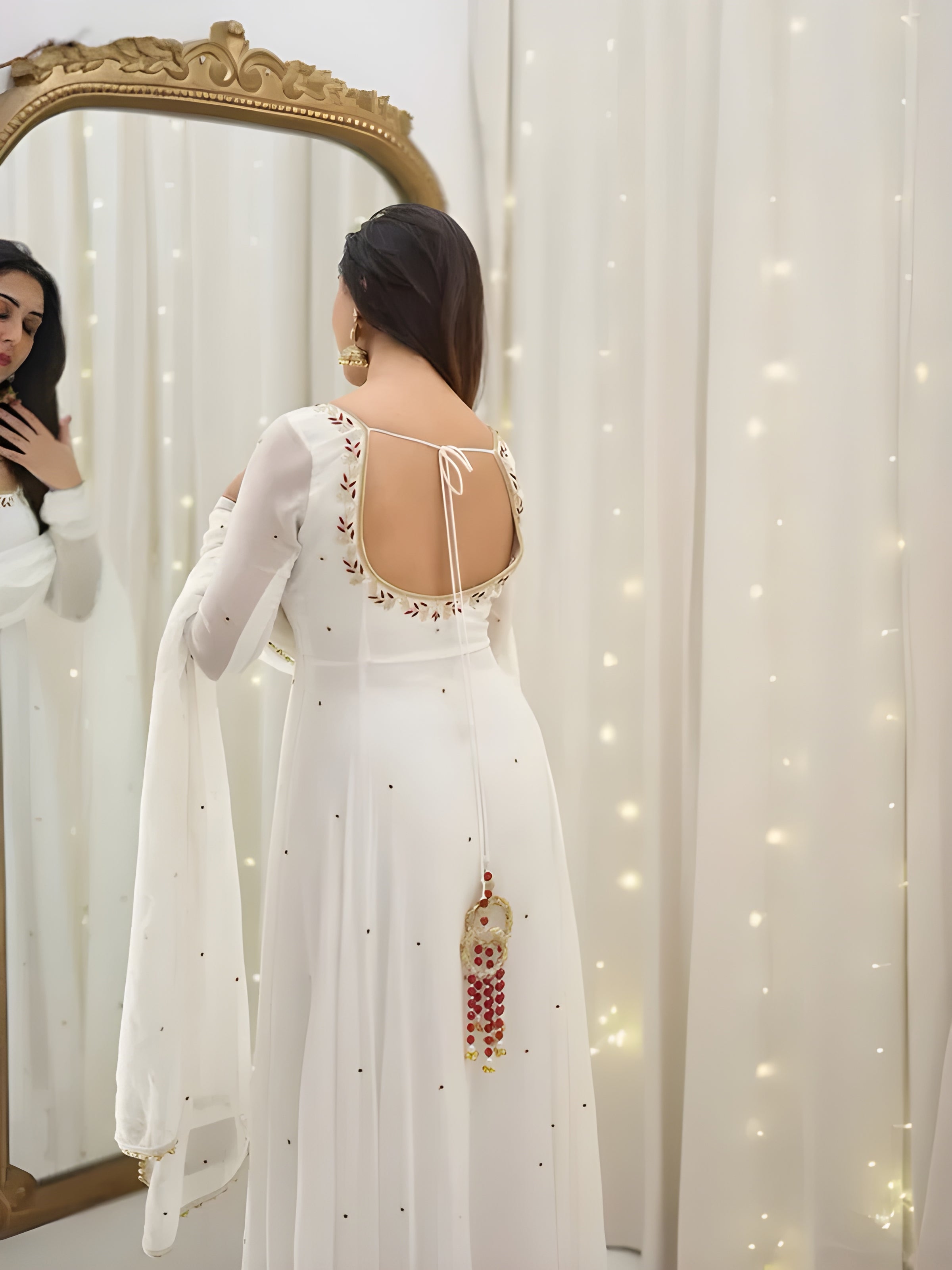 Woman in a white dress with intricate designs standing in front of a mirror.
