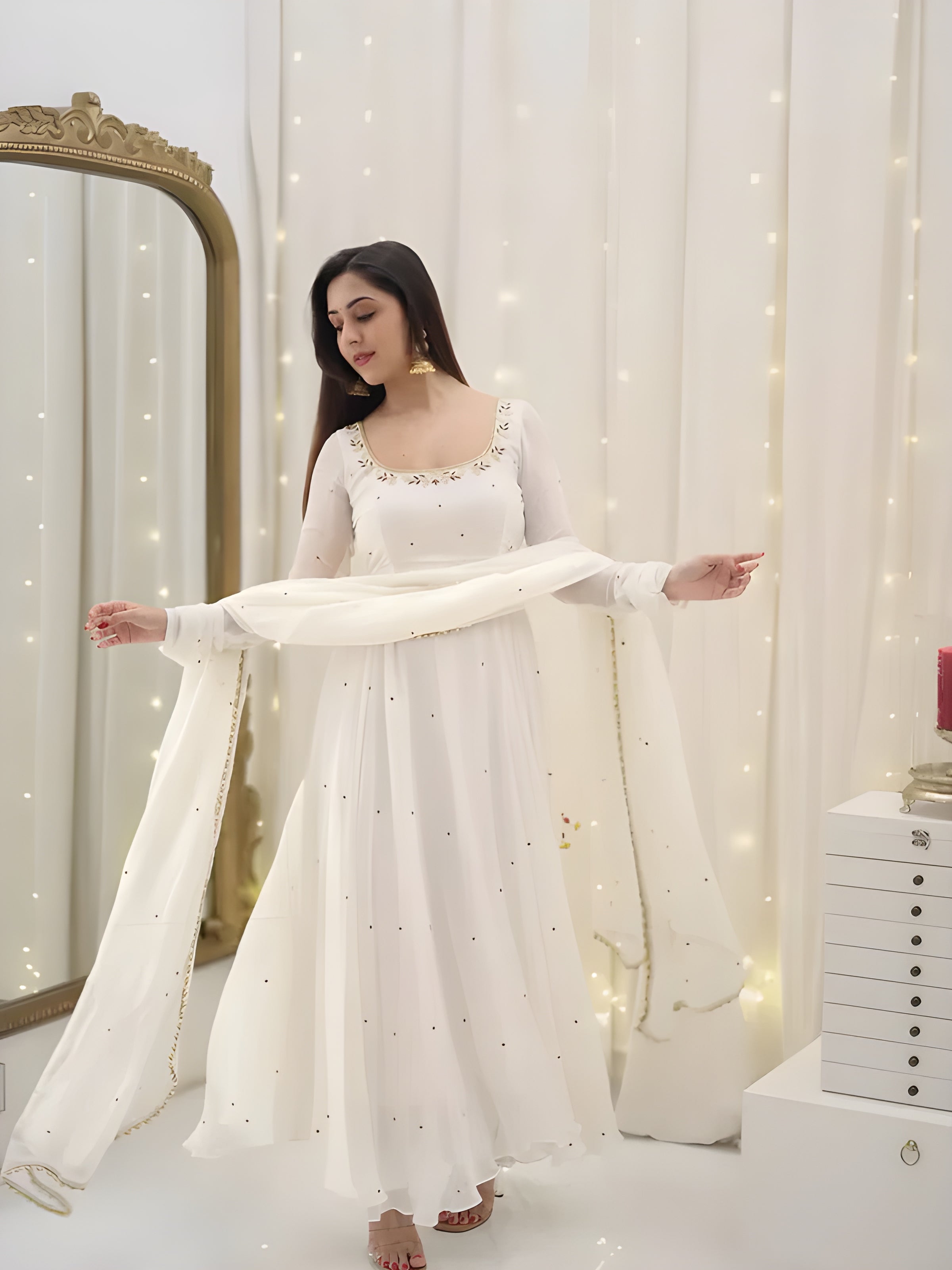 Woman in a white traditional outfit standing in front of a mirror with decorative lights.