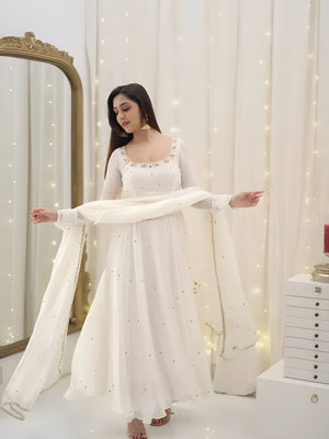 Woman in a white traditional outfit standing in front of a mirror with decorative lights.