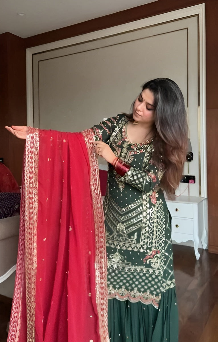 Woman holding a red dupatta with intricate patterns in a room.