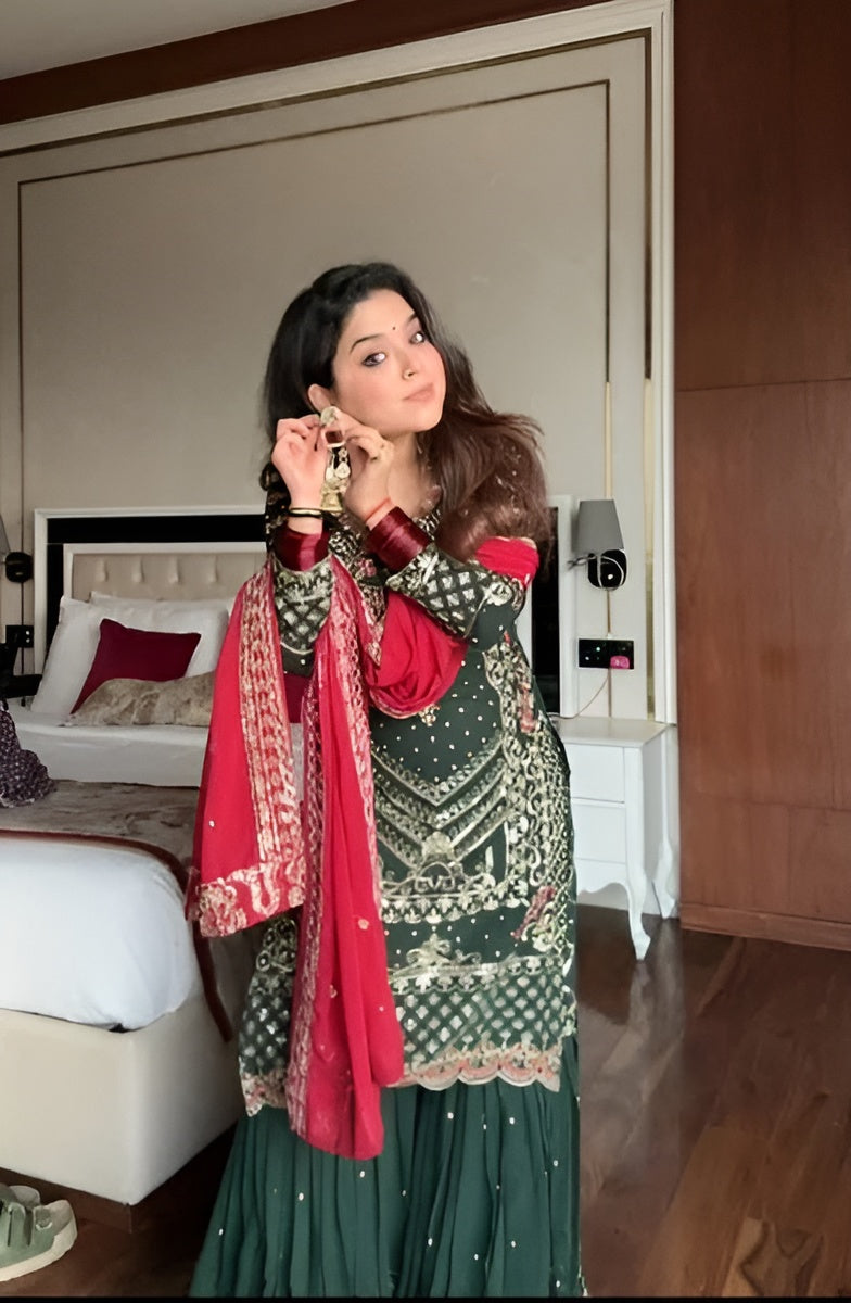 Woman in a green traditional outfit with a red dupatta in a bedroom setting