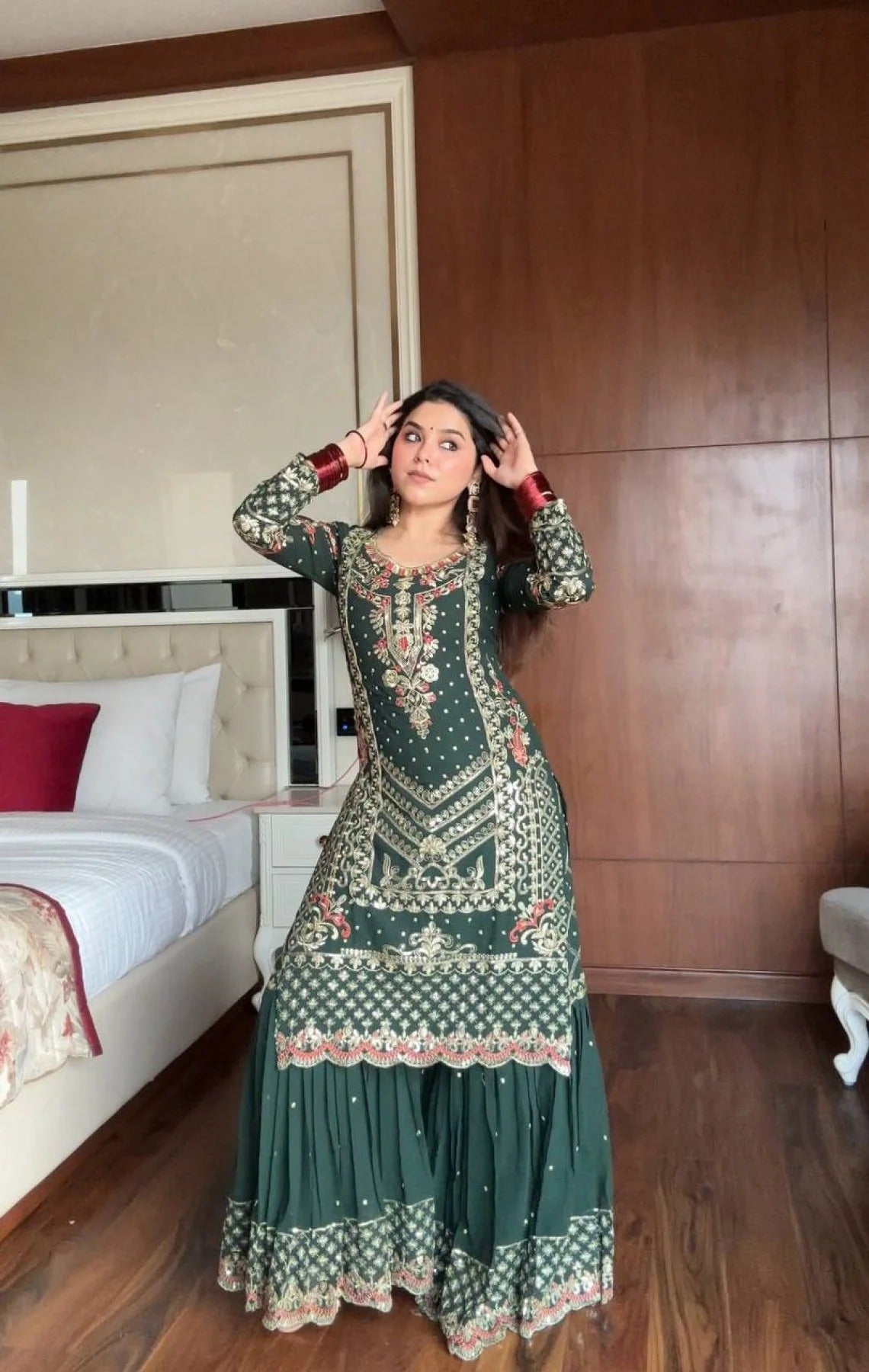 Woman in a green traditional outfit standing in a bedroom.