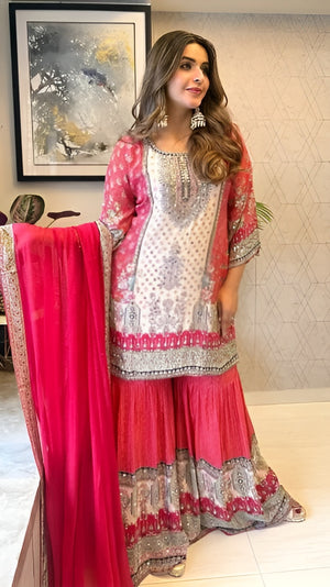 Woman in a traditional outfit with pink and white patterns, holding a red dupatta.