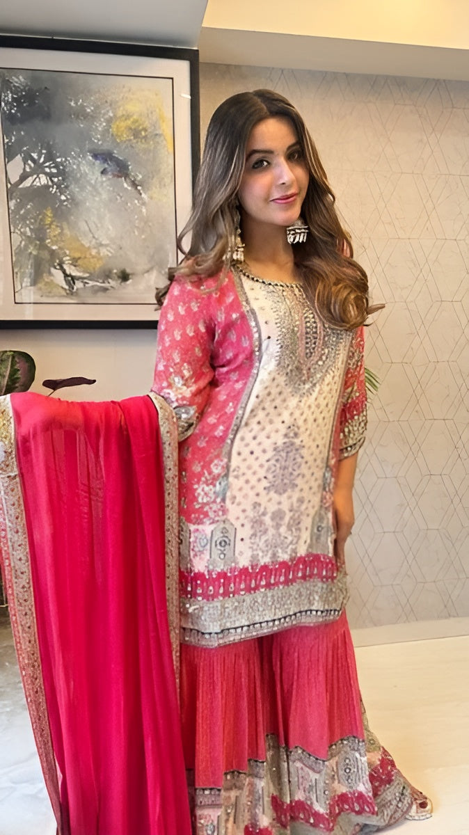Woman in a traditional outfit with pink and white elements, standing indoors.