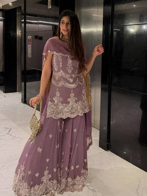 Woman in a purple traditional outfit with intricate designs standing in front of an elevator.