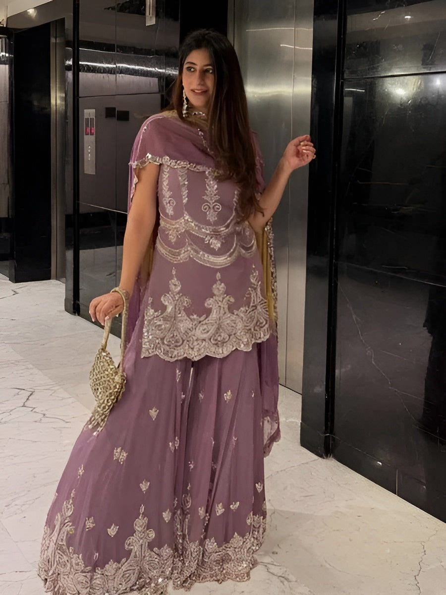 Woman in a purple traditional outfit with intricate designs standing in front of an elevator.
