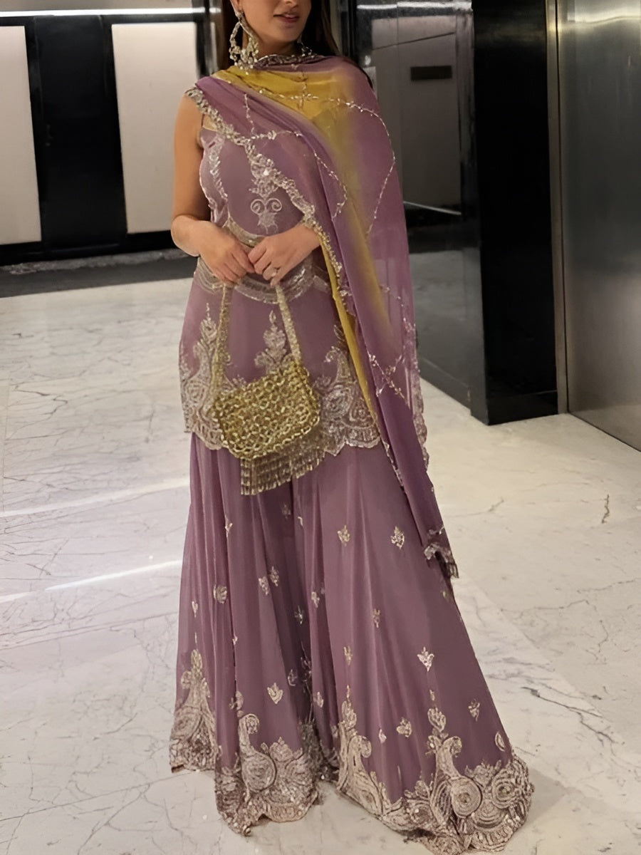 Person wearing a purple embroidered outfit with a yellow dupatta in an indoor setting.