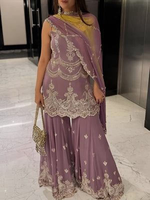 Woman wearing a purple embroidered saree with a yellow blouse in an indoor setting.