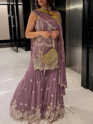 Woman in a purple embroidered saree with a gold handbag in an indoor setting