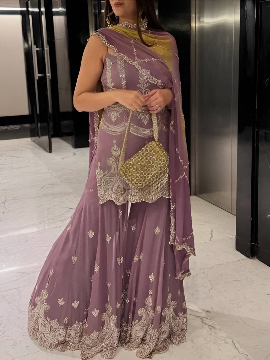 Woman in a purple embroidered saree with a gold handbag in an indoor setting