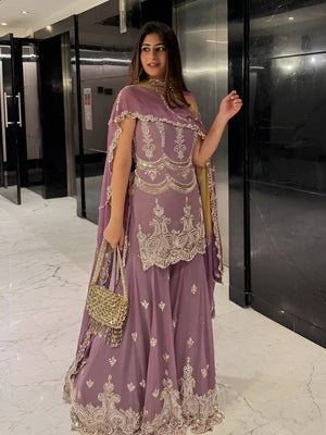 Woman in a purple embroidered outfit with gold details in an indoor setting