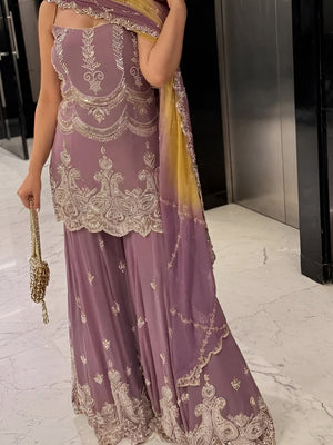 Person wearing a purple saree with gold embroidery in an indoor setting