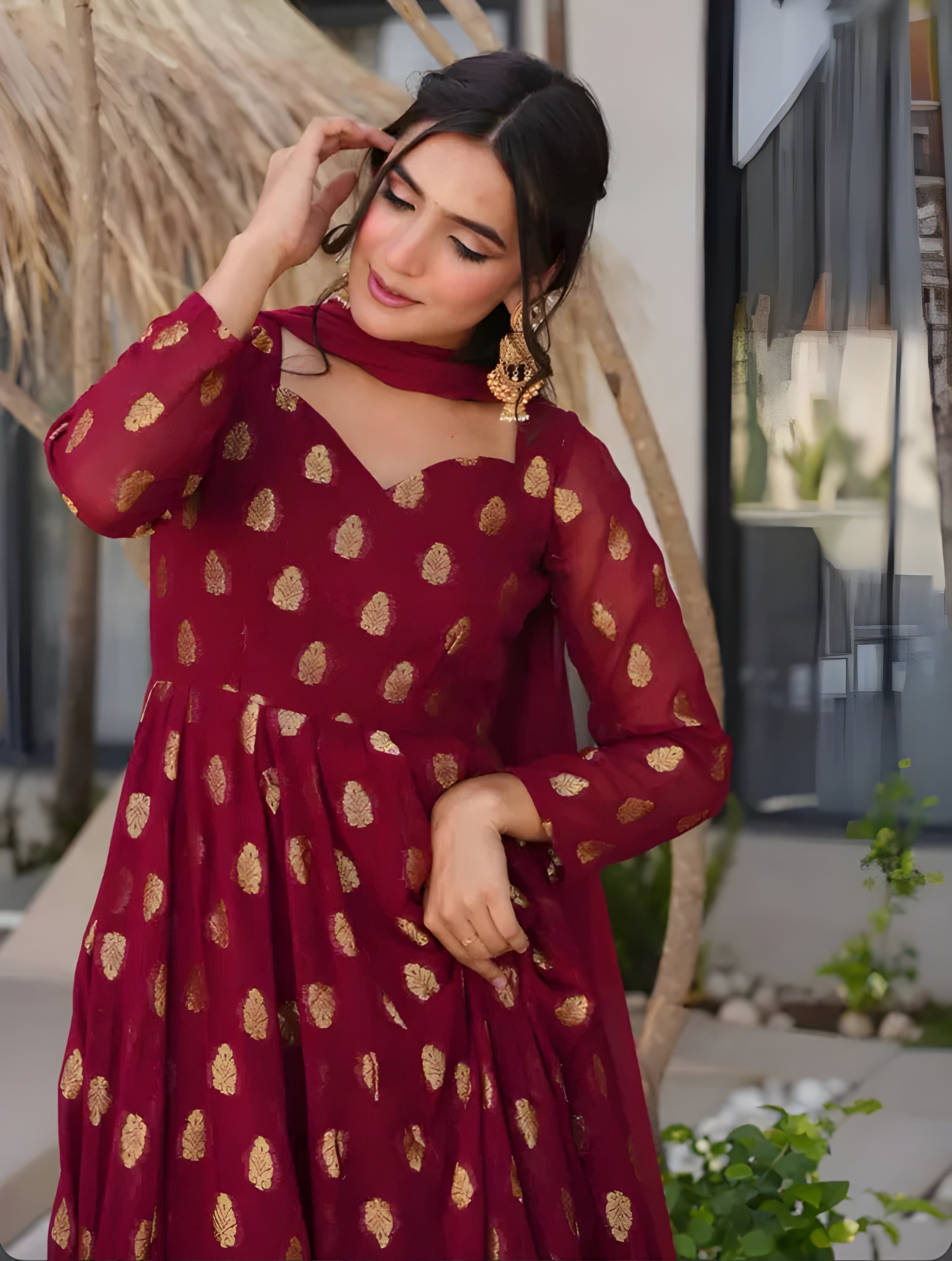 Woman wearing a red dress with gold patterns outdoors.