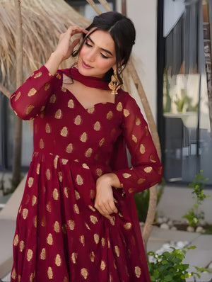 Woman wearing a red dress with gold patterns outdoors.