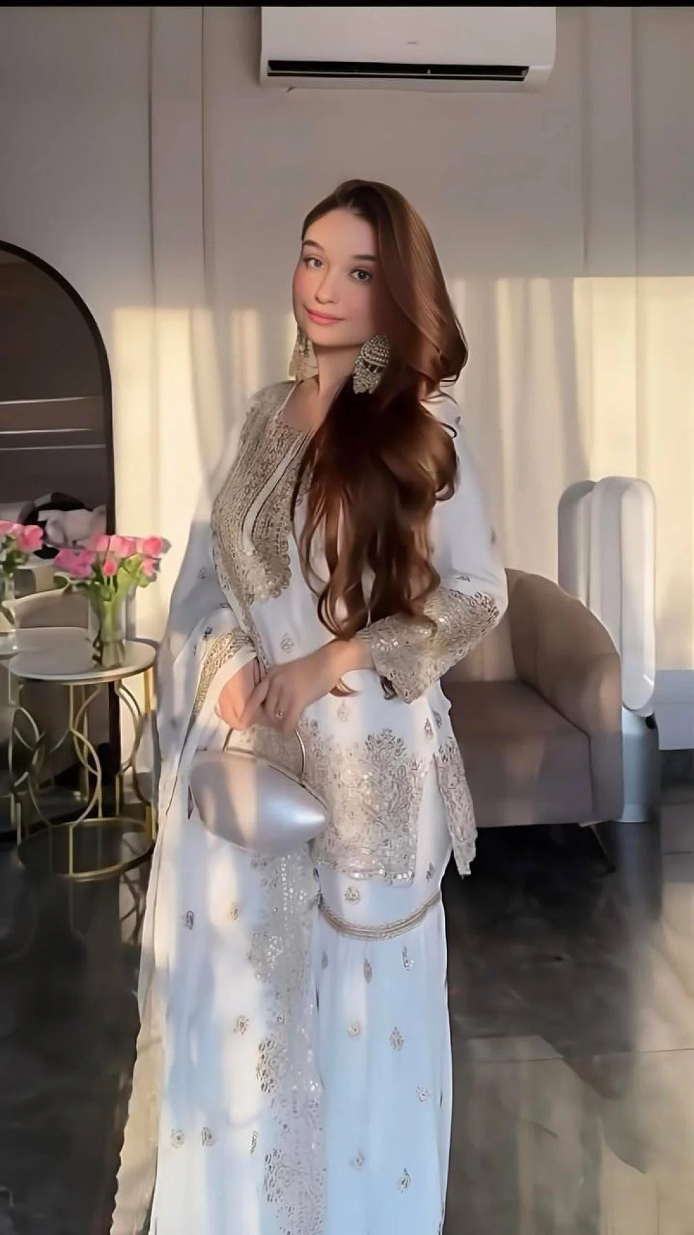 Woman in a light blue traditional outfit with silver embroidery in an indoor setting.