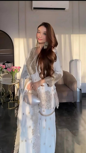 Woman in a light blue traditional outfit with silver embroidery in an indoor setting.