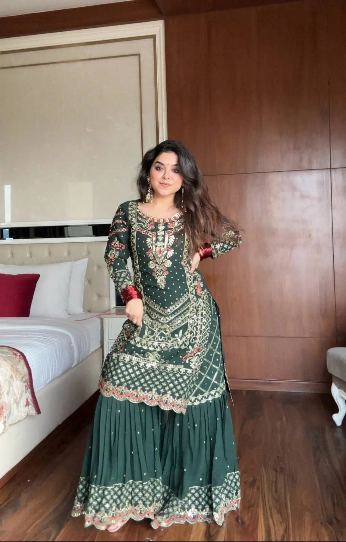Woman in a green traditional outfit standing in a bedroom.